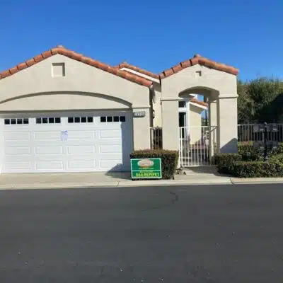 Front view of a single-story home with a white garage door and terracotta roof, featuring a sign for a plumbing service on the lawn, indicating recent or ongoing home maintenance work.